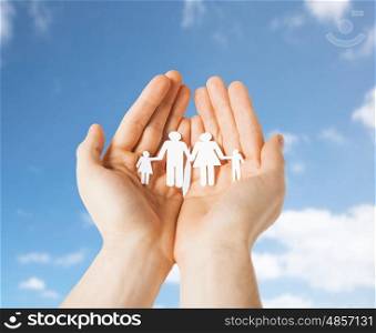 people concept - close up of male hands holding paper family pictogram over blue sky and clouds background. close up of hands holding paper family pictogram