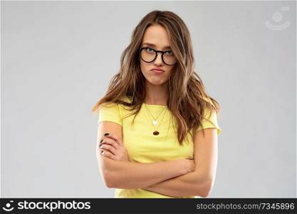 people concept - frowning young woman or teenage girl in yellow t-shirt and glasses pouting over grey background. young woman or teenage girl in glasses pouting