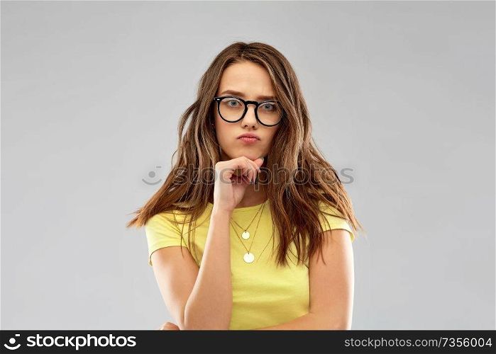 people concept - frowning young woman or teenage girl in yellow t-shirt and glasses over grey background. frowning young woman or teenage girl in glasses