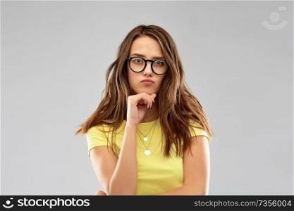 people concept - frowning young woman or teenage girl in yellow t-shirt and glasses over grey background. frowning young woman or teenage girl in glasses