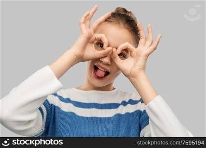 people concept - funny teenage girl looking through finger glasses over grey background. funny teenage girl looking through finger glasses