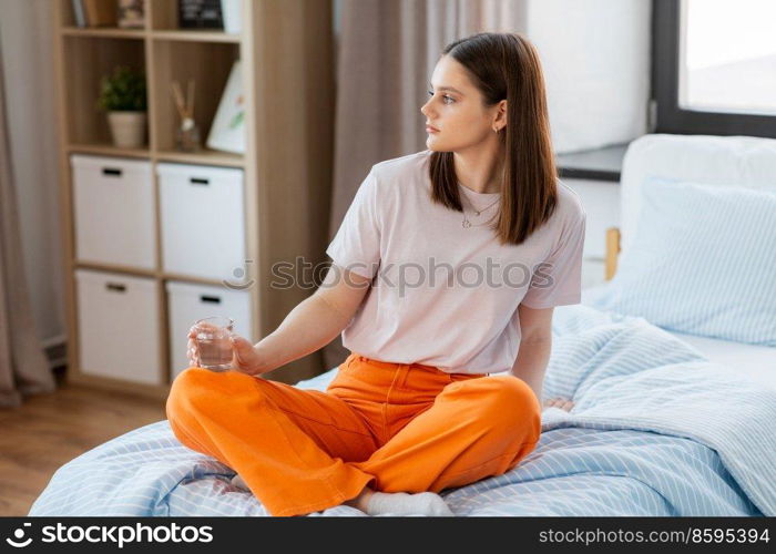 people concept - girl with glass of water sitting on bed at home. girl with glass of water sitting on bed at home