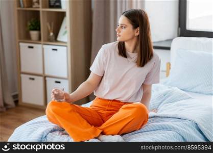 people concept - girl with glass of water sitting on bed at home. girl with glass of water sitting on bed at home