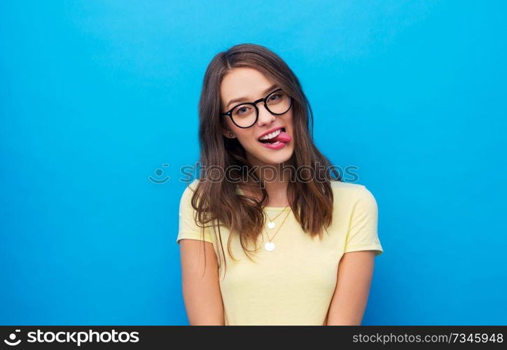 people concept - goofy young woman or teenage girl in yellow t-shirt and glasses over bright blue background. young woman or teenage girl in glasses