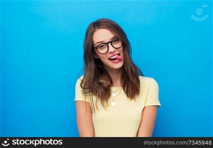 people concept - goofy young woman or teenage girl in yellow t-shirt and glasses over bright blue background. young woman or teenage girl in glasses