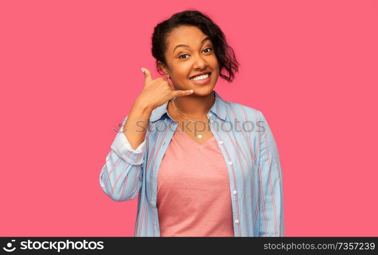 people concept - happy african american young woman making phone calling gesture over pink background. african american woman making phone call gesture