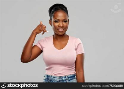 people concept - happy african american young woman making phone calling gesture over pink background. african american woman making phone call gesture