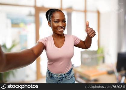 people concept - happy african american young woman taking selfie and showing thumbs up over office background. african woman taking selfie and showing thumbs up
