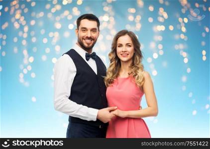 people concept - happy couple in party clothes over holiday lights on blue background. happy couple in party clothes
