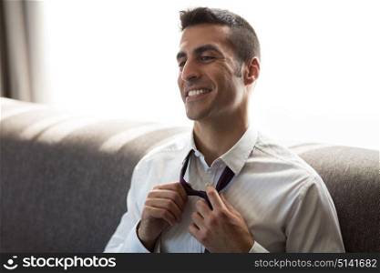 people concept - happy smiling businessman taking off his tie at hotel room. happy businessman taking off his tie at hotel room