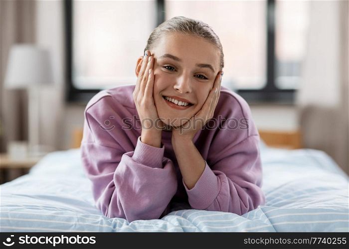 people concept - happy smiling girl lying on bed at home. happy smiling girl lying on bed at home