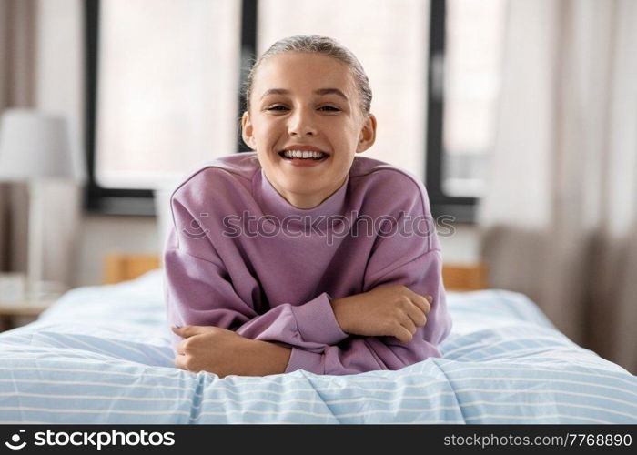 people concept - happy smiling girl lying on bed at home. happy smiling girl lying on bed at home