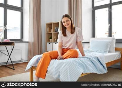 people concept - happy smiling girl with glass of water sitting on bed at home. girl with glass of water sitting on bed at home