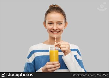 people concept - happy smiling teenage girl in pullover holding glass of orange juice with paper straw over grey background. smiling teenage girl holding glass of orange juice