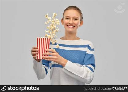 people concept - happy smiling teenage girl in pullover with popcorn in striped bucket over grey background. smiling teenage girl with popcorn