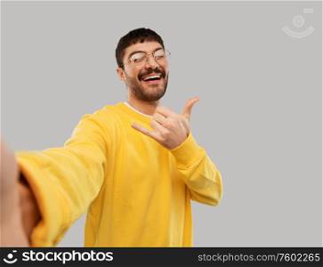 people concept - happy smiling young man in glasses and yellow sweatshirt making selfie over grey background. happy young man in yellow sweatshirt making selfie