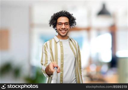 people concept - happy smiling young man in glasses taking picture with selfie stick over office background. man taking picture with selfie stick at office