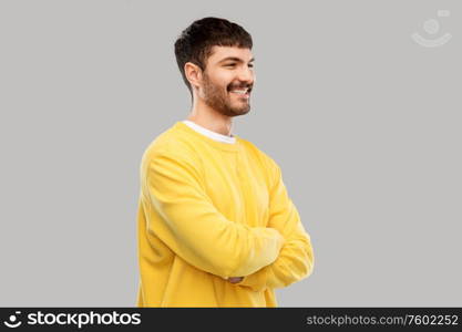 people concept - happy smiling young man in yellow sweatshirt with crossed arms over grey background. young man in yellow sweatshirt with crossed arms