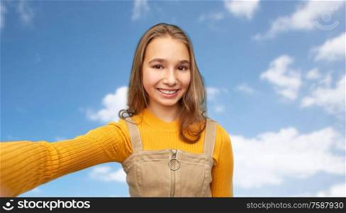people concept - happy smiling young teenage girl taking selfie over blue sky and clouds background. happy teenage girl taking selfie over sky