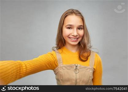 people concept - happy smiling young teenage girl taking selfie over grey background. happy teenage girl taking selfie