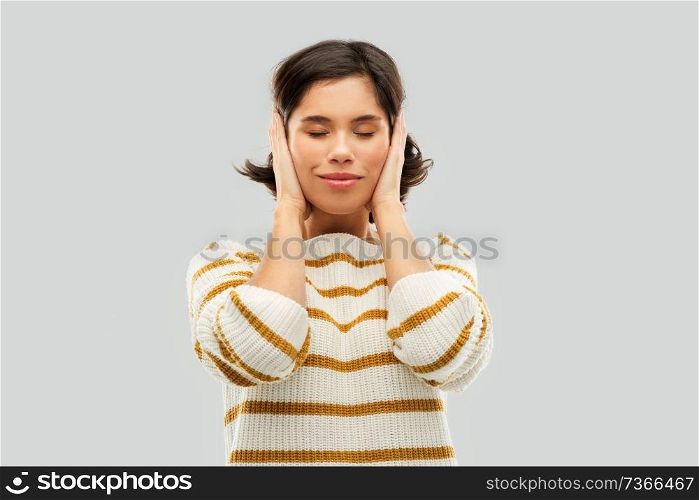 people concept - happy smiling young woman in striped pullover closing ears by hands over grey background. happy woman in pullover closing ears by hands