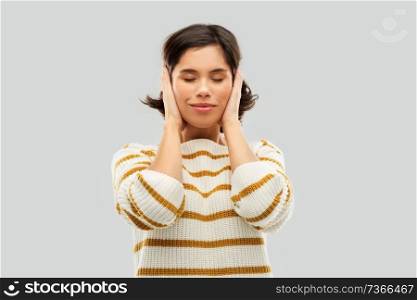 people concept - happy smiling young woman in striped pullover closing ears by hands over grey background. happy woman in pullover closing ears by hands