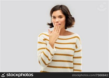 people concept - happy smiling young woman in striped pullover covering mouth by hand and giggling over grey background. happy woman covering mouth by hand and giggling