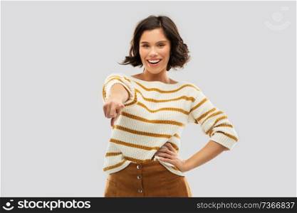 people concept - happy smiling young woman in striped pullover pointing finger to you over grey background. happy smiling woman pointing finger to you