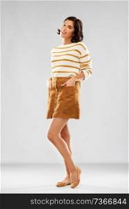 people concept - happy smiling young woman in striped pullover, short skirt and ballet flat shoes posing over grey background. young woman in striped pullover, skirt and shoes