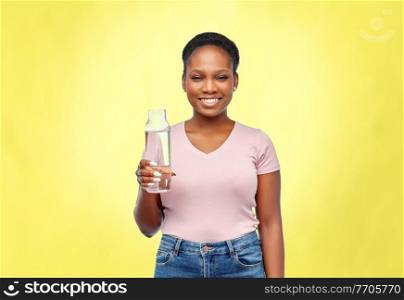 people concept - portrait of happy smiling young african american woman drinking water from reusable glass bottle over illuminating yellow background. happy african woman drinks water from glass bottle
