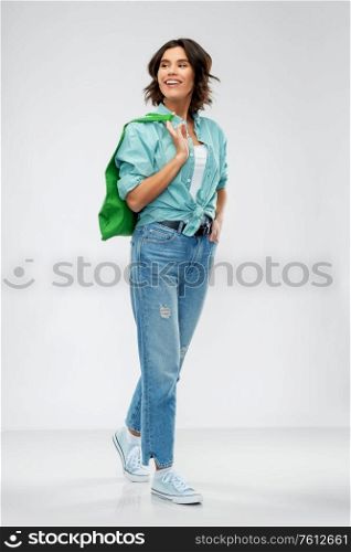 people concept - portrait of happy smiling young woman in turquoise shirt and jeans walking with green reusable canvas bag for food shopping on grey background. woman with reusable canvas bag for food shopping