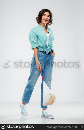 people concept - portrait of happy smiling young woman in turquoise shirt and jeans walking with bananas in reusable string bag over grey background. happy woman with bananas in reusable string bag