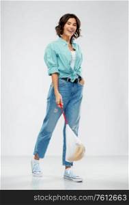 people concept - portrait of happy smiling young woman in turquoise shirt and jeans walking with bananas in reusable string bag over grey background. happy woman with bananas in reusable string bag