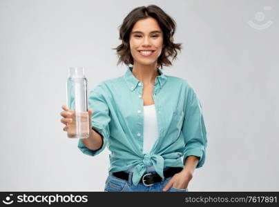 people concept - portrait of happy smiling young woman in turquoise shirt holding water in reusable glass bottle grey background. smiling young woman holding water in glass bottle
