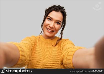 people concept - portrait of happy smiling young woman with pierced nose taking selfie over grey background. smiling woman with pierced nose taking selfie