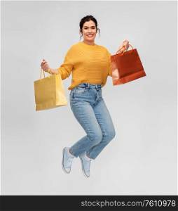 people concept - portrait of happy smiling young woman with pierced nose with shopping bags jumping over grey background. happy young woman jumping with shopping bags