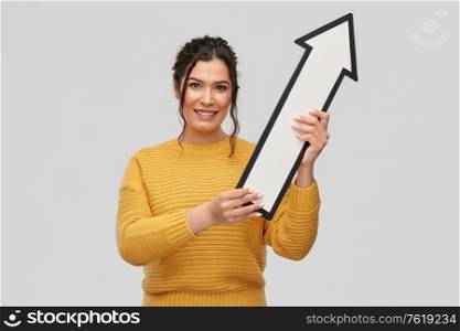 people concept - portrait of happy smiling young woman with pierced nose holding big white thick arrow showing up over grey background. smiling young woman with big white upward arrow