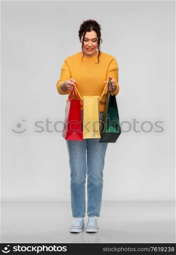 people concept - portrait of happy smiling young woman with pierced nose with shopping bags over grey background. happy smiling young woman with shopping bags