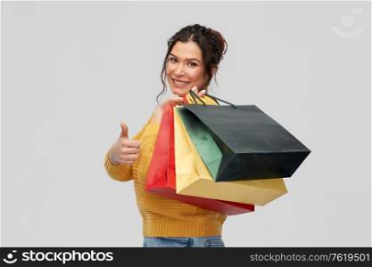 people concept - portrait of happy smiling young woman with pierced nose with shopping bags showing thumbs up over grey background. smiling woman with shopping bags showing thumbs up