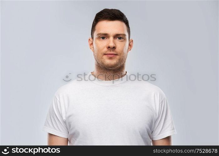 people concept - portrait of serious young man in white t-shirt over grey background. portrait of serious young man in white t-shirt