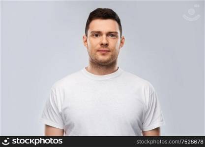 people concept - portrait of serious young man in white t-shirt over grey background. portrait of serious young man in white t-shirt