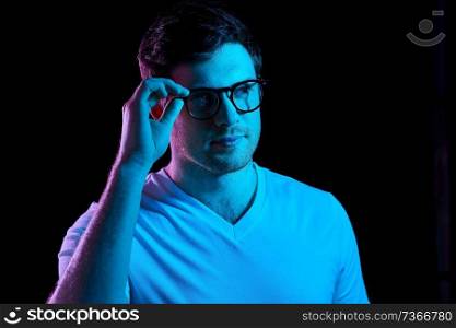 people concept - portrait of young man in glasses and t-shirt over ultra violet neon lights in dark room. man in glasses over neon lights in dark room