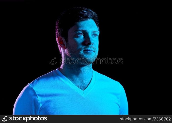 people concept - portrait of young man in t-shirt over ultra violet neon lights in dark room. portrait of man over neon lights in dark room