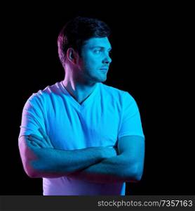 people concept - portrait of young man in t-shirt with crossed arms over ultra violet neon lights in dark room. man with crossed arms over neon lights in darkness