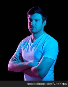 people concept - portrait of young man in t-shirt with crossed arms over ultra violet neon lights in dark room. man with crossed arms over neon lights in darkness