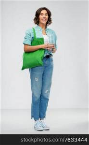 people concept - portrait of young woman with green reusable canvas bag for food shopping and glass bottle of water over grey background. woman with bag for food shopping and glass bottle