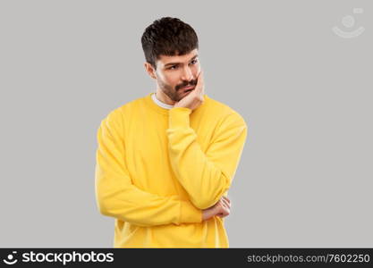 people concept - sad young man in yellow sweatshirt thinking over grey background. sad young man in yellow sweatshirt thinking