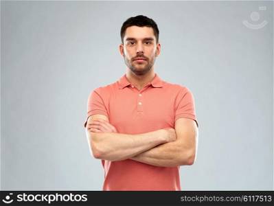 people concept - serious young man in polo t-shirt with crossed arms over gray background. young man with crossed arms over gray background