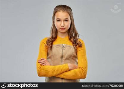 people concept - serious young teenage girl with crossed arms over grey background. serious young teenage girl with crossed arms