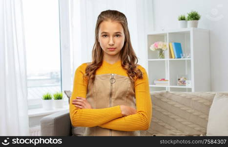 people concept - serious young teenage girl with crossed arms over home background. serious teenage girl with crossed arms at home